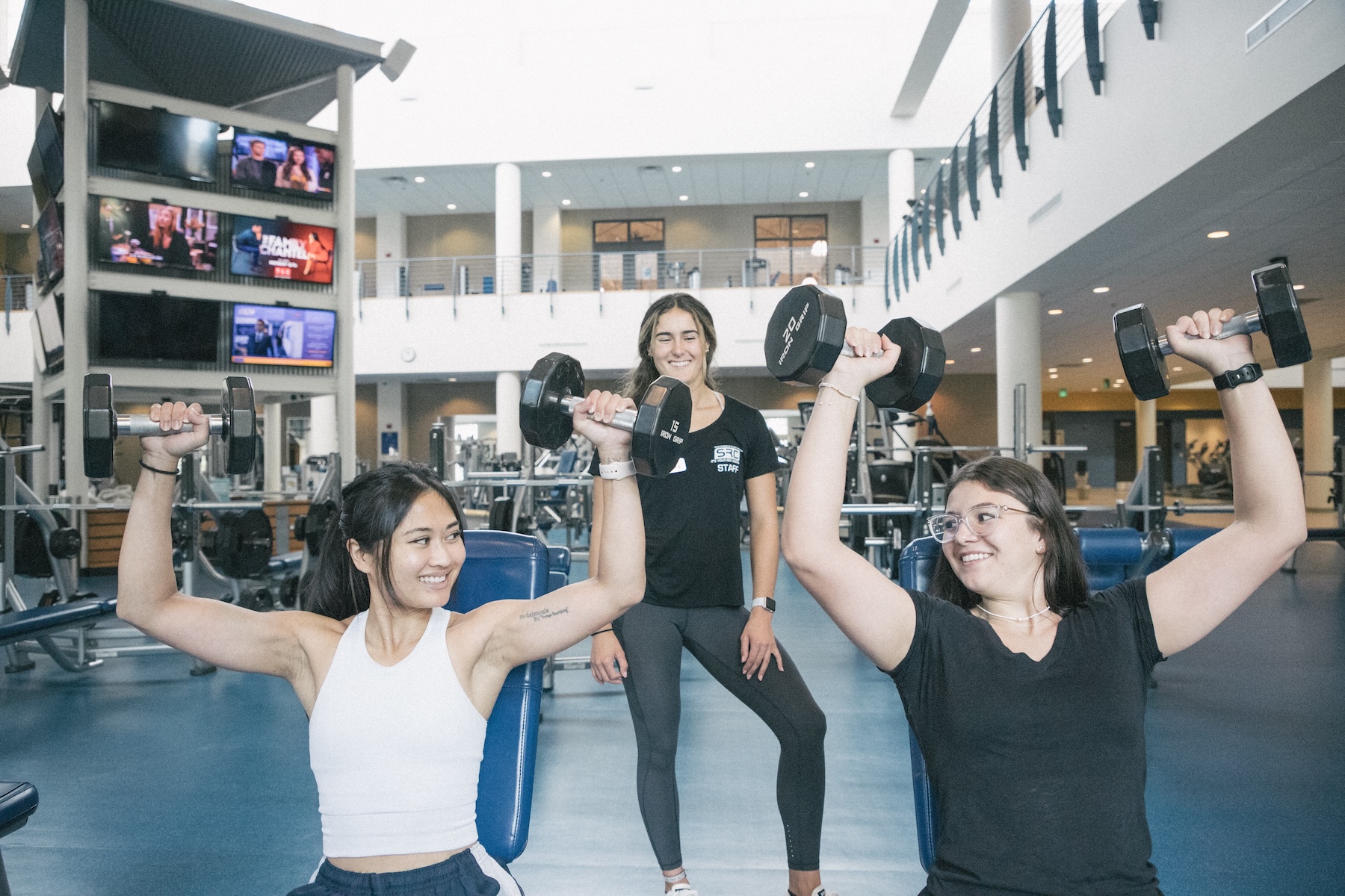 Women lifting dumbbells while a personal trainer watches