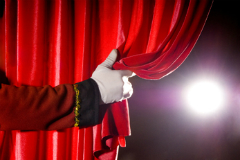 gloved hand pulling back a stage curtain
